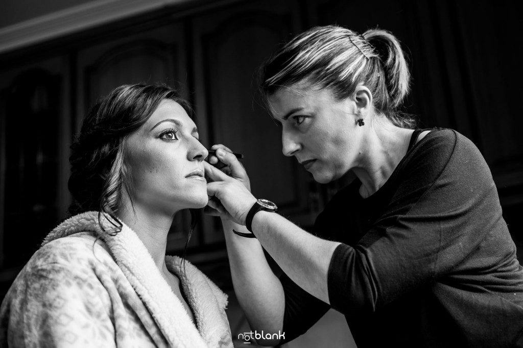 Boda en Salceda de Caselas. La maquilladora le está haciendo la aya del ojo a la novia. Reportaje realizado por Notblank fotógrafos de boda en Galicia.