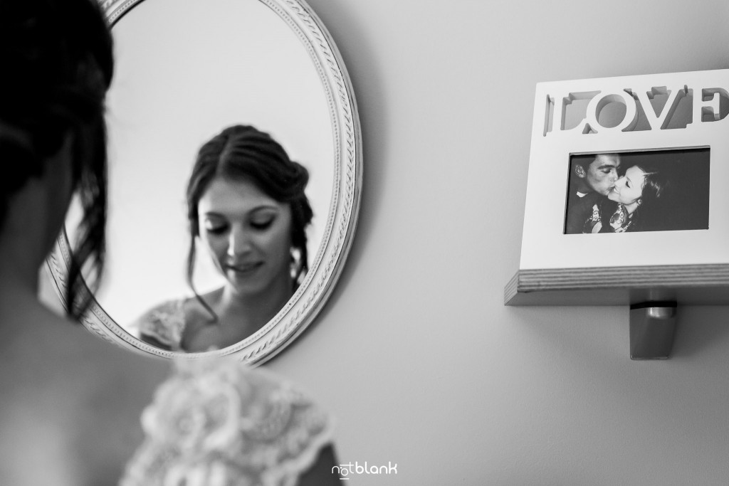 Boda en Salceda de Caselas. La novia se prepara delante de un espejo en su habitación. A su derecha tiene un marco de fotos con una foto suya y su futuro marido. El marco de fotos pone LOVE (AMOR) en grande. Reportaje realizado por Notblank fotógrafos de boda en Galicia.