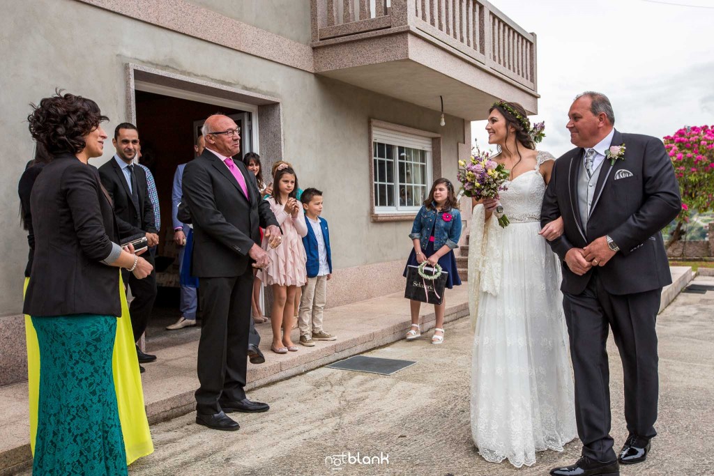 Boda en Salceda de Caselas. La novia del brazo del padre saluda a los invitados en casa de los padres antes de emprender camino hacia la iglesia. Reportaje realizado por Notblank fotógrafos de boda en Galicia.