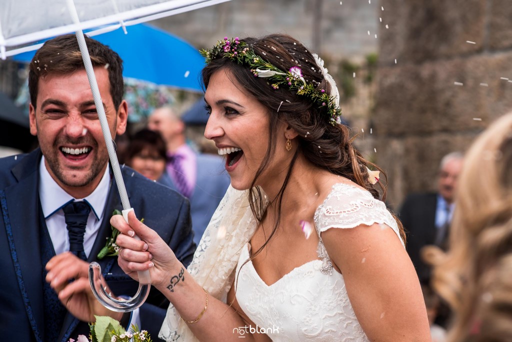 Boda en Salceda de Caselas. Expresión de los novios tras la gran lluvia de arroz a la salida de la iglesia. La novia sostiene un paraguas para refugiarse de la lluvia de arroz. Reportaje realizado por Notblank fotógrafos de boda en Galicia.